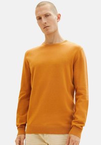 Suéter de punto naranja con cuello redondo y mangas largas. Presenta un dobladillo ribeteado y puños. Textura suave con un discreto detalle de marca.