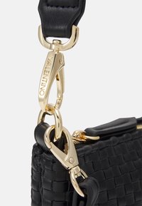 Svart vävd läderväska med guldhardware, tryckknappar och ett slätt axelband. Anmärkningsvärd textur kontrasterar med de blanka metalldetaljerna.