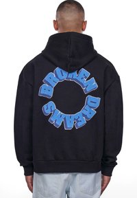 Black hoodie featuring a circular blue embroidered design with the text "BROKEN DREAMS" prominently displayed on the back.