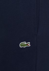 Marineblaue Baumwollstoffe mit strukturierter Oberfläche und einem grünen, mit weiß umrandeten Krokodil-Logo auf der linken Seite gestickt.