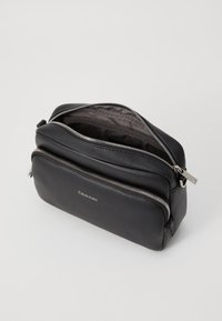 Borsa in pelle nera con una finitura testurizzata, dotata di due scomparti con zip e un accento in metallo argentato. Logo Calvin Klein sul fronte.