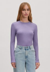 Langmouwtop in licht lila ribstof, met een ronde halslijn en een getailleerde snit, gecombineerd met hooggeremde lichtblauwe jeans.