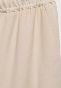 Tissu beige avec une texture froncée le long d'une ceinture élastique cousue, montrant un matériau tissé lisse en gros plan.