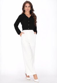 Fekete, hosszú ujjú, gombos felső, amelyet magas derekú, fehér, bő szárú nadrággal párosítanak. Mindkét ruhadarab sima textúrájú és szabott kialakítású.