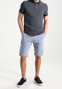 Granatowa polo z wzorem i krótkim rękawem, połączona z jasnoniebieskimi szortami. Dodatkiem są ciemnoniebieskie trampki.