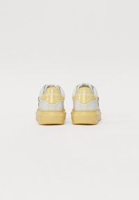 Weiße und gelbe Sneakers mit einer glatten Lederoberfläche, runder Form, gepolstertem Schaft und Logodetail an der Ferse. Gummisohle.