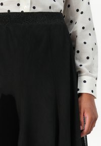 Black skirt with a textured surface and a glittery waistband. Paired with a white shirt featuring black polka dots. Close-up view.