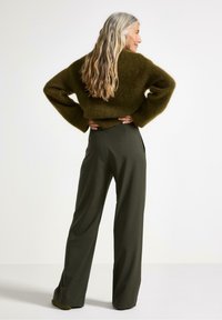 Maglione verde oliva, a maglia larga, con maniche ampie, abbinato a pantaloni dritti in verde scuro a vita alta, caratterizzati da una texture liscia.