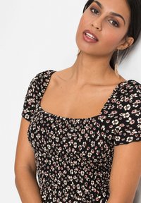 Robe noire à imprimé floral, dotée d'un décolleté carré, d'un corsage smocké et de courtes manches ballons avec des motifs de fleurs blanches et rouges.