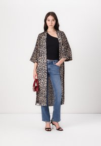 Leopardprint kimono van lichtgewicht stof, met wijde mouwen en een open voorkant, gecombineerd met een zwarte top en blauwe jeans, geaccessoireerd met een rode handtas.