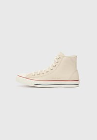 Beige Canvas-Hochschnittsneaker mit weißer Gummisohle, roten und blauen Streifen, Metallösen für die Schnürsenkel und "Chuck Taylor"-Logo an der Seite.