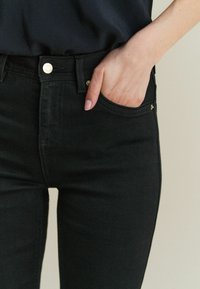 Mustad denim püksid kitsase lõikega, millel on kuldne riistvara, esipidemed ja peened õmblusdetailid.