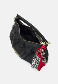 Svart läderhandväska med guld blixtlås, rynkad design och en kontrasterande silkescarf med djärva textaccenter i röd och svart.