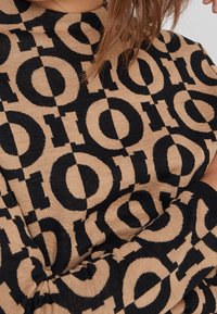Sweter z dzianiny z geometrycznym wzorem w czerni i beżu z wyraźnymi okrągłymi motywami, okrągłym dekoltem i ściągaczami.