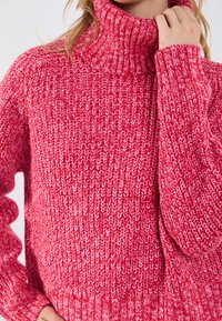 Maglione lavorato a maglia di un vivace colore rosa, con colletto alto a costine, caratterizzato da un motivo testurizzato e maniche morbide.