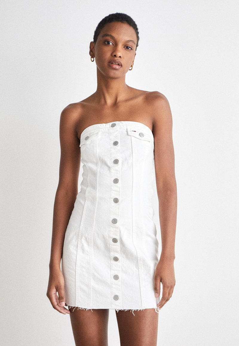 Λευκό τζιν φόρεμα χωρίς τιράντες με κλείσιμο μπροστά με κουμπιά, πλαϊνές ραφές και φθαρμένο στρίφωμα. Διαθέτει ασημένια κουμπιά και εφαρμοστή σιλουέτα.