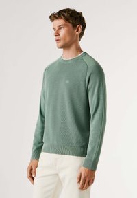 Zelený pletený sveter s okrúhlym výstrihom, textúrovanou látkou, rebrovanými manžetami a lemom, s jemným logom na hrudi.