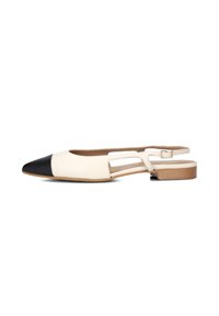 Platte slingback schoen in crèmekleurig leer met een puntige zwarte neus; is voorzien van uitsparingen aan de zijkanten en een kleine bruine hak.
