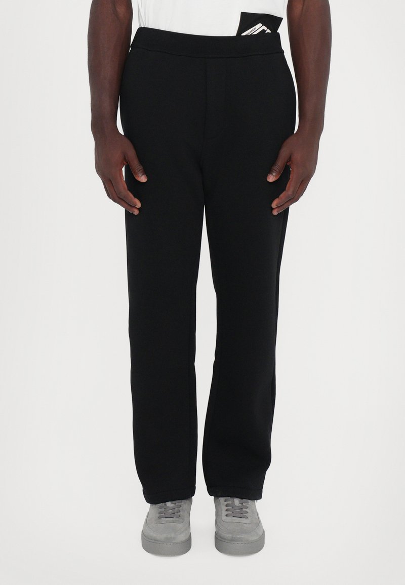 Schwarze Sportleggings mit elastischem Bund, geraden Beinen und glatter Textur. Bemerkenswerte Details sind eine versteckte Tasche am Bund.