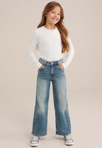 Bela srajca z dolgimi rokavi, v kombinaciji z visokim pasom, svetle modre široke hlače, ki imajo klasičen design s petimi žepi in zaponko.