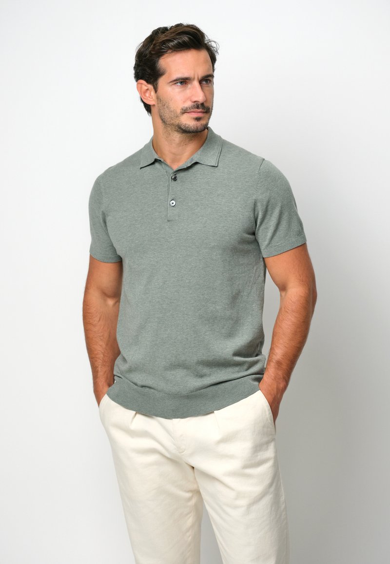 Grön kortärmad polo skjorta i mjukt tyg, med ribbad krage och placket med två knappar, i kombination med ljusa byxor.