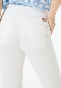Witte damesbroek met een gladde textuur, voorzien van achterzakken met diagonale stiksels en zilverkleurige knopen. Logo label op de tailleband.
