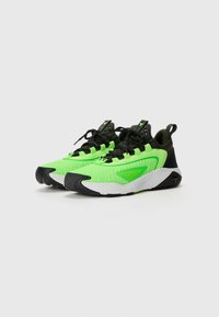 Sneakers atletici verde brillante con tomaia testurizzata, dettagli neri e suola bianca. Presentano un sistema di allacciatura e un dettaglio del logo sul tallone.