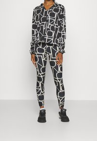 Schwarz-weiße Activewear-Ausstattung mit einem Kapuzen-Zip-Up-Top und Leggings, hergestellt aus einem glatten, dehnbaren Stoff.