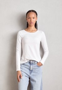 White long-sleeve shirt with a round neckline, paired with light blue high-waisted jeans. Simple design and smooth cotton texture.