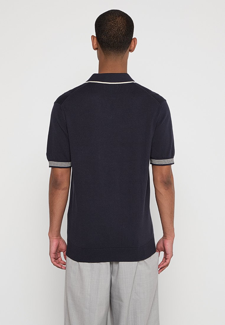Chemise polo bleu marine à manches courtes avec un col côtelé, présentant des accents rayés sur les manches et un tissu doux et texturé.