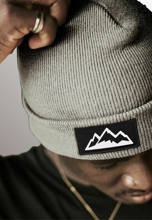 Gray ribbed knit beanie featuring a black patch with white mountain graphic. Close-up view, highlighting texture and design details.