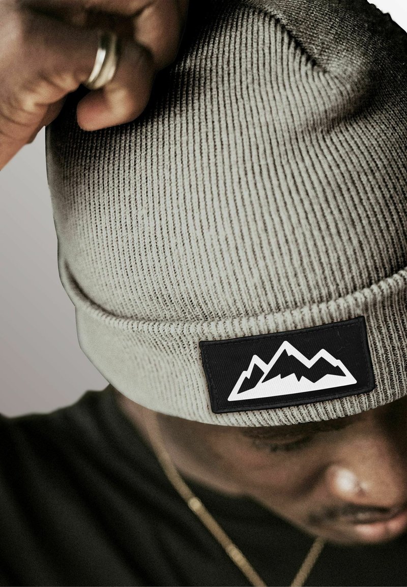 Gray ribbed knit beanie featuring a black patch with white mountain graphic. Close-up view, highlighting texture and design details.