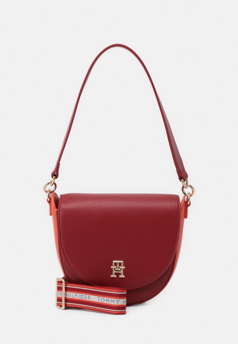 Porte-monnaie en cuir rouge à la forme arrondie, arborant un logo doré, une bandoulière rayée ajustable et une texture lisse.