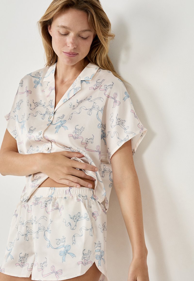Korte mouwen pyjama set van een lichtroze stof met speelse katten- en lintpatronen. De shorts hebben een elastische tailleband voor comfort.
