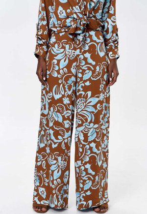Braune, floral gemusterte Hosen mit lockerer Passform, die blaue Blumen zeigen. Das Material wirkt glatt und wird mit einer Bluse zum Binden vorne kombiniert.