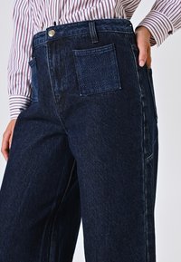 Donkerblauwe denim broek met een hoge taille, voorzien van een zijzak en een achterpatch zak, met een gestructureerde stof en een rechte pasvorm.