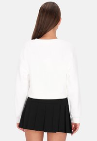 Fehér, crop fazonú pulóver hosszú ujjakkal, bordázott mandzsettákkal és kerek nyakkivágással, fekete pliszírozott miniszoknyával párosítva. Tiszta dizájn, modern megjelenés.
