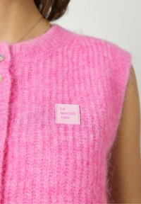 Roosa kudumivest, millel on soonikkoes, nööpide sulgemine ja ristkülikukujuline logoiket, millel on kiri "LA MAISON AMV."