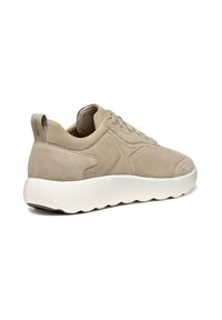 Sneaker en suède beige avec une semelle extérieure blanche arrondie, présentant un design minimaliste, des coutures discrètes et une languette à l'arrière.
