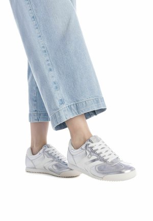 Zapatillas deportivas plateadas y blancas con textura suave, diseño de paneles en contraste y suela de goma, combinadas con unos jeans cortos de color azul claro.