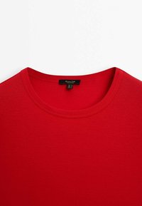 T-shirt rouge à col rond avec une étiquette de marque noire visible cousue à l'intérieur du col.