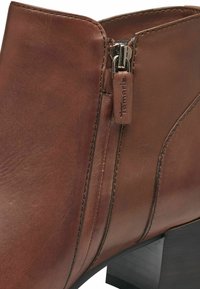 Botte de cheville en cuir marron avec une fermeture éclair, dotée d'un talon empilé, de coutures décoratives et d'une étiquette logo Tamaris fixée à la fermeture.