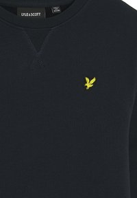 Marineblå bomulds sweatshirts med rund hals, der har et lille gult broderet ørne-logo på brystet og ribbet struktur på manchetterne.