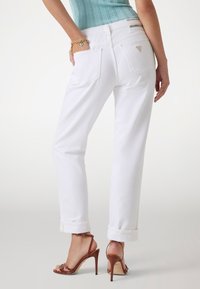 Jeans in denim bianco con una vestibilità rilassata, orli risvoltati e tasche posteriori. Presenta un accento con logo metallico sulla vita.