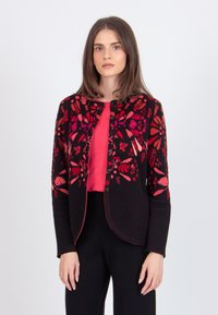 Black cardigan with bright red floral embroidery, round neckline, open front, and long sleeves, paired with a red top and black pants.