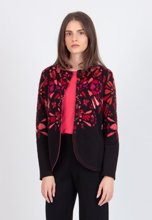Cardigan nero con ricami floreali rossi brillanti, colletto tondo, apertura frontale e maniche lunghe, abbinato a una maglietta rossa e pantaloni neri.