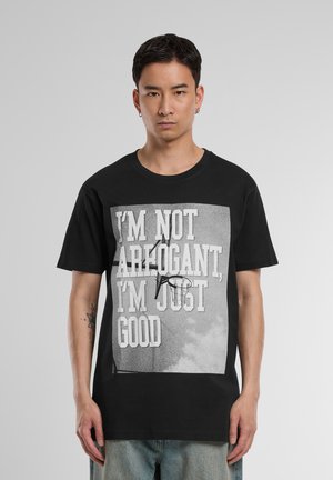 T-shirt en coton noir avec un imprimé graphique portant le texte "JE NE SUIS PAS ARROGANT, JE SUIS JUSTE BON" et un design de panier de basket. Manches courtes.