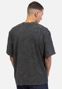 Tekstureret grå t-shirt med et præget paisley-mønster, kortærmede og en afslappet pasform. Bagsiden viser designets detaljer klart.