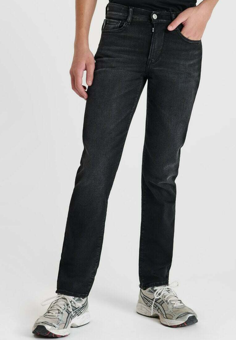 Jean en denim noir avec une coupe ajustée, design à cinq poches et un léger délavage. Associés à des chaussures de sport gris clair.