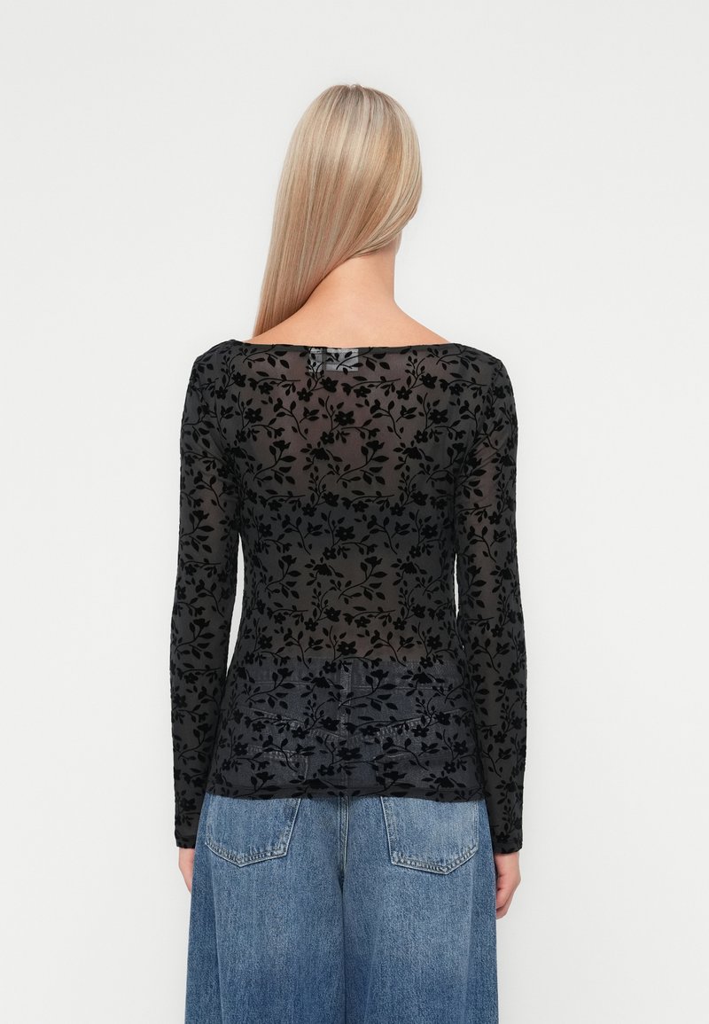 Schwarzes Langarmoberteil mit einem transparenten Blumenmuster, glatter Textur und einem Bootsausschnitt, kombiniert mit blauen hoch taillierten Jeans.